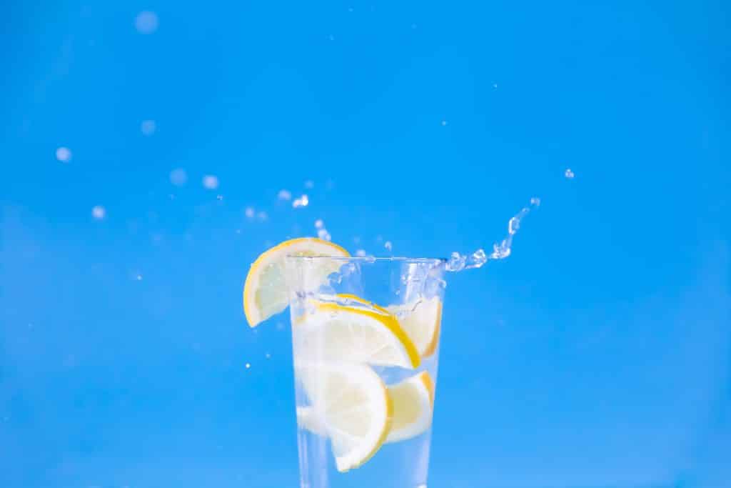voda s limunom, kriške limuna, plava podloga, čaša vode