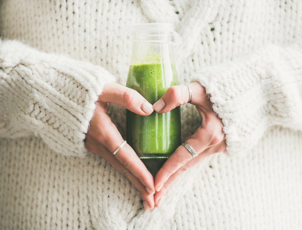 žena drži zeleni smoothie ispred sebe s rukama u obliku srca