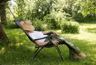 Žena odmara u ležaljci na travi ispod drveta, simbolizira proljetni umor i potrebu za opuštanjem na svježem zraku.
