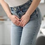 Woman in jeans clutching her lower abdomen, possibly indicating pain or discomfort, commonly associated with urinary tract infection (UTI) or bladder issues.