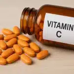 Bočica vitamina C s prolivenim narančastim tabletama na drvenoj podlozi – dodatak prehrani za imunitet i zdravlje.