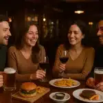Veselo društvo muškaraca i žena u pubu, uz pivo i vino na stolu, s burgerima, biftekom i pomfritom.