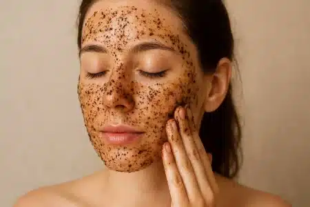 Mlada žena nanosi piling za lice od kave. Zatvorenih očiju i blagog osmijeha, prstima nježno masira lice.