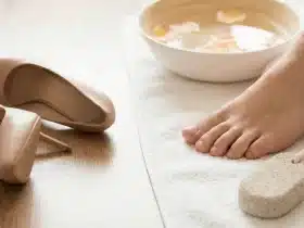 Stopalo na ručniku uz zdjelu za namakanje, plovućac i kremu za njegu kože – kućna njega stopala i uklanjanje kurjeg oka.