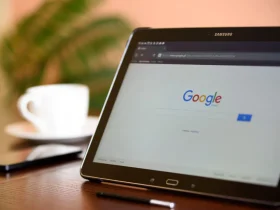 Tablet sa otvorenom Google početnom stranicom na stolu, uz šalicu kave, pametni telefon i olovku.